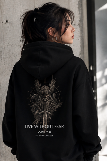 A woman shown from behind wearing a black hoodie with a large graphic print on the back. The print features a dark gothic illustration of a winged skull holding a sword, with the text 'LIVE WITHOUT FEAR', 'ODIN'S WILL', and 'EST.